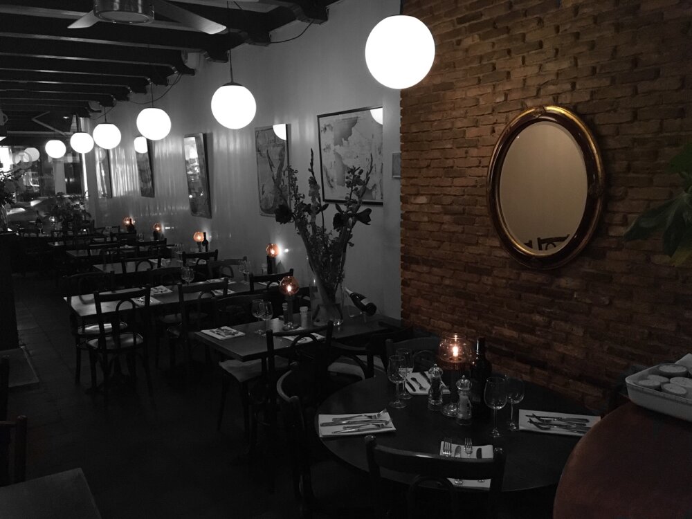 Het interieur van Quartier Latin met bolle hanglampen, kaarslicht en een bakstenen muur